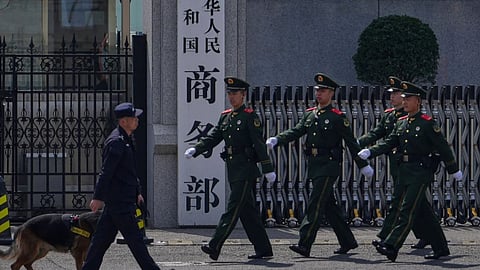 Paramilitary soldiers and a police officer with a sniffer dog march past the main entrance gate of China’s Ministry of Commerce, in Beijing, on April 3, 2025. 