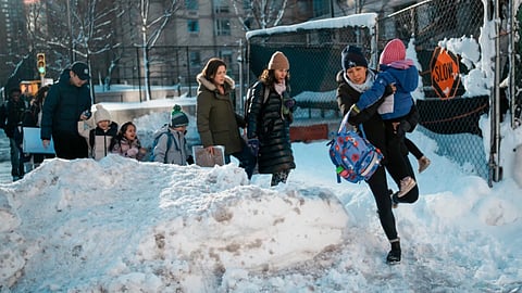 A woman carries a child over piles of plowed snow as she walks a girl to school, 