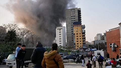 Residents watch as smoke rises from a nearby building during an Israeli strike in central Beirut, Lebanon, Thursday, March 12, 2026