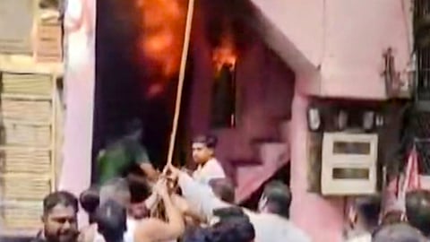 People gather as flames and thick smoke billow from a house following a fire incident, in Surat