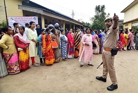 A police official assists people waiting in a queue to cast votes during the Assam Assembly elections, at a polling station at Bonda, in Guwahati, Thursday, April 9, 2026.