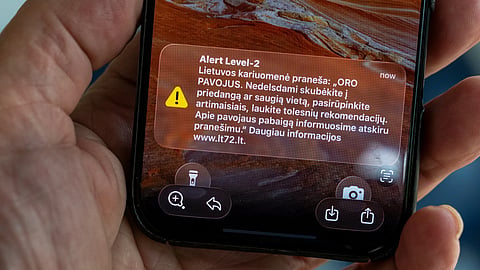 The phone shows the received message "The Lithuanian military reports: "AIR DANGER. Hurry to cover or a safe place without delay, take care of your loved ones, wart for further recommendations''