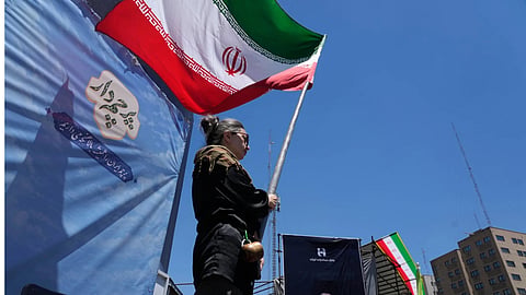 A woman waves an Iranian flag during a pro-government campaign as a portrait of the slain Supreme Leader Ayatollah Ali Khamenei, who was killed in U.S. and Israeli strikes