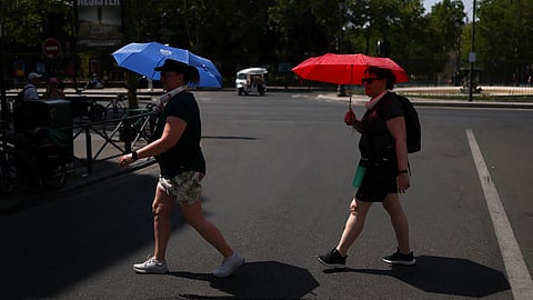 People cross the road while sheltering themselves from the sun under umbrellas in central Paris during high temperatures amid a heatwave in Paris, France, on June 27, 2026.