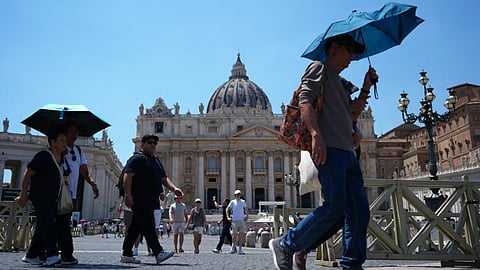 People shade from the sun under umbrellas as they walk through St Peter's Square at the Vatican