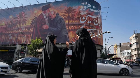 Women talk in front of a banner with graphic depicting the slain Iranian Supreme Leader Ayatollah Ali Khamenei kissing head of the late commander of Iran’s Revolutionary Guard expeditionary Quds Force, Gen. Qassem Soleimani, who was killed in a U.S. drone attack in 2020 in Iraq, as they wait for the green light to cross an intersection in downtown Tehran, Iran