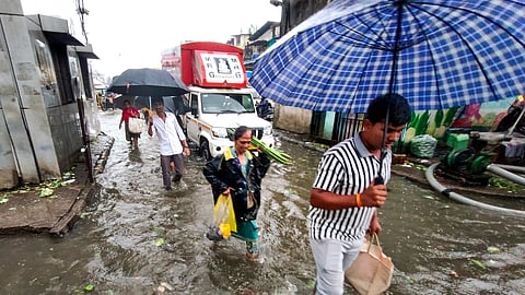 Pedestrians make their way through a waterlogged road amid rainfall, in Navi Mumbai