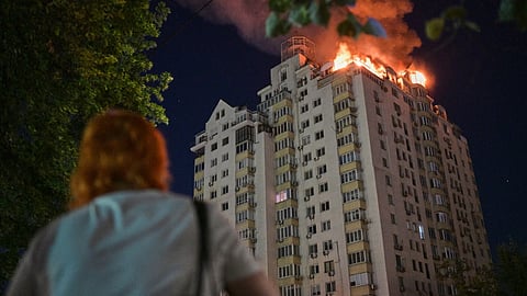 A woman looks at an apartment building burning after a Russian missile attack in Kyiv, Ukraine