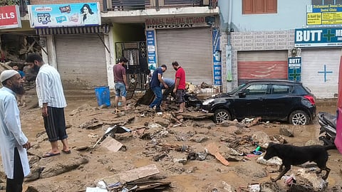 People inspect debris and damaged vehicles after flash floods triggered by incessant rainfall and cloudbursts caused widespread destruction in Doda district