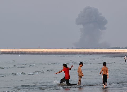 Three boys play in the shallow waters of the Strait of Hormuz, as a plume of smoke rises from an explosion in the background, off Bandar Abbas, Iran, Monday, July 13, 2026. 
