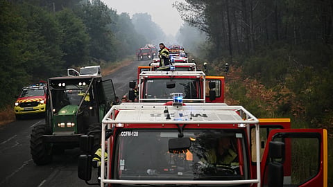 A firefighter stands on a truck on a road near Lacanau, southwestern France, Saturday, July 25, 2026, as wildfires rage in the area.