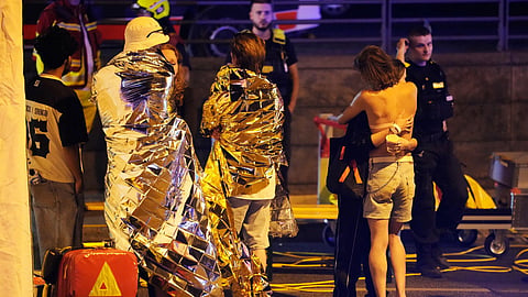 Two people embrace near others wearing thermal blankets as they stand near emergency personnel in Berlin, early Sunday, July 26, 2026, following the cancellation of Christopher Street Day festivities. 