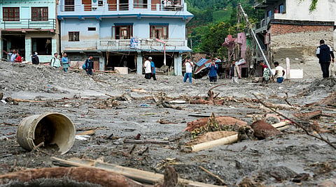 An area covered in thick mud and debris as people walk past damaged structures following the devastating flash floods at Devighat village, in Nuwakot district, Nepal, Friday, Aug. 28, 2026