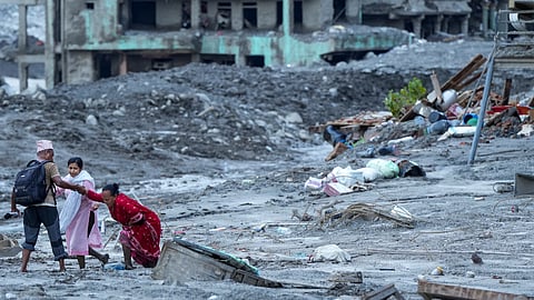 A man gives support to an elderly near an area covered in mud and debris in the aftermath of flash floods, at Trishuli market
