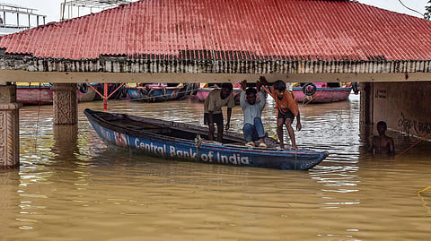 People duck on a wooden boat as they move on a partially submerged area after heavy rains, near Assi Ghat in Varanasi, Tuesday, Sept. 1, 2026.