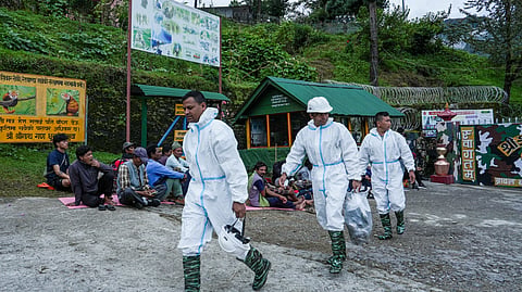 Security personnel wearing protective gear walk past flood-affected people sitting outside an army base camp in the aftermath of the recent flash floods, in Rasuwa district, Nepal, Wednesday, Sept. 2, 2026.
