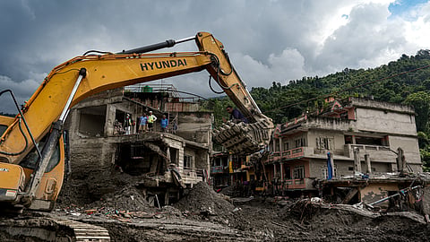 An excavator clears mud, sludge, and debris from damaged buildings along the Trishuli River, at Devighat, in Nuwakot district, Nepal