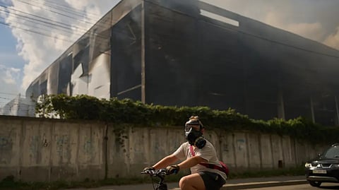 A local resident wears a gas mask as he rides a bicycle past a partially destroyed warehouse after a Russian drone attack in Brovary on the outskirts of Kyiv, Ukraine