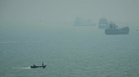 A motorboat travels past commercial vessels anchored amid haze in the Strait of Hormuz off Bandar Abbas, Iran.