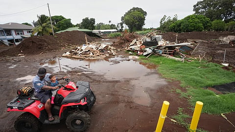 A man rides with his son near where a home was destroyed during last month's Hurricane Lala, as floodwaters from Hurricane Nolo