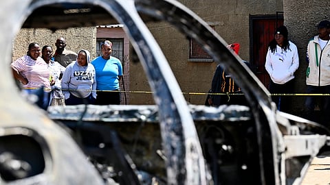 Community members stand at scene of a mass shooting on Saturday night when suspects opened fire at a bar in Wedela township, southwest of Johannesburg, South Africa