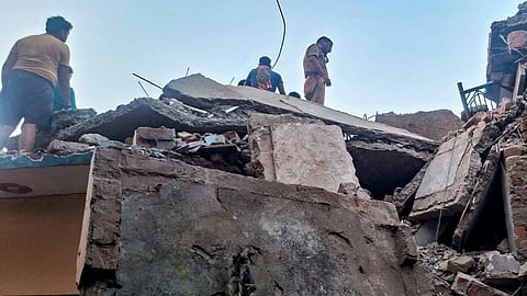 A police official and people stand on a damaged structure after a domestic LPG cylinder exploded, causing a two-storey building to collapse, at Malwan, in Fatehpur district