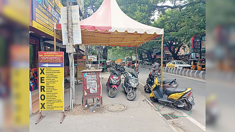 Shops, parked vehicles and advertisement boards occupy pavement on one side of the road