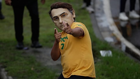 A supporter of opposition presidential candidate Flavio Bolsonaro wears a mask of his father, former President Jair Bolsonaro, during a campaign rally a day ahead of the country's general election, in Campo Grande, Rio de Janeiro state.