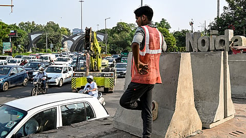 A worker stands near newly placed concrete jersey barriers as traffic slows down at the Chilla Border, in New Delhi