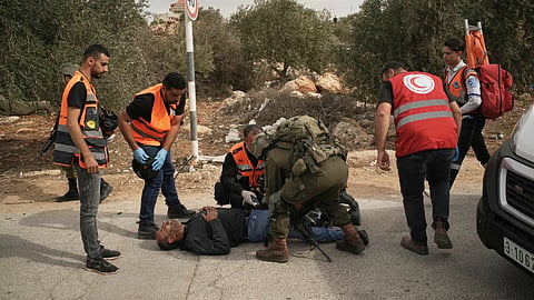 Palestinian medics and an Israeli soldier attend to a Palestinian man shot by Israeli soldiers following a settler attack on Palestinians harvesting olives in the West Bank village of Abu Falah, Friday, Oct. 16, 2026.