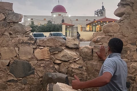  A man looks through a gap in a stone wall toward a Greek Orthodox church where gunmen opened fire during a funeral hours earlier in Hamoud village, in Jordan’s Karak governorate, Friday, Oct. 23, 2026. 