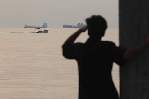  A man looks out over the water as a small boat passes cargo ships anchored in the Strait of Hormuz off Bandar Abbas, Iran, early Saturday, Oct. 24, 2026.