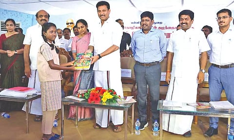 Minister Anbil Mahesh Poyyamozhi presenting books to migrant students after launching ‘Tamil Mozhi Karpom’ scheme in Tirupur on Tuesday