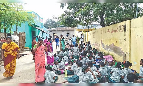 Students sitting on the road in front of their school as parents locked premises in Alangayam on Monday.
