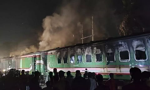 People stand near a burning passenger train at Gopibagh in Dhaka on Friday. (AP)