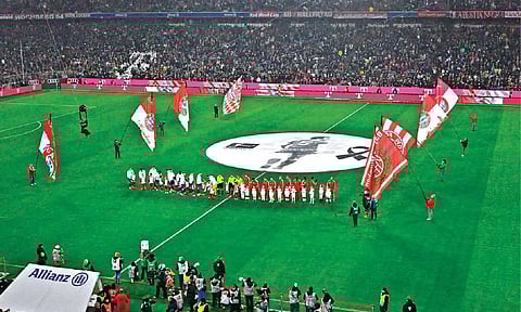 Bayern Munich players line up on the pitch with a banner of Franz Beckenbauer ahead of kick-off