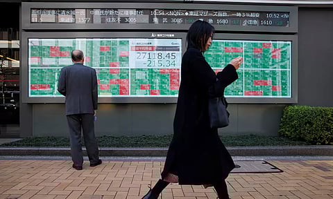 A woman walks past a man examining an electronic board showing Japan's Nikkei average and stock quotations outside a brokerage (Reuters)
