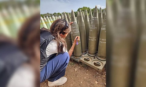 UN Nikki Haley kneeling and writing on a shell with a purple marker pen