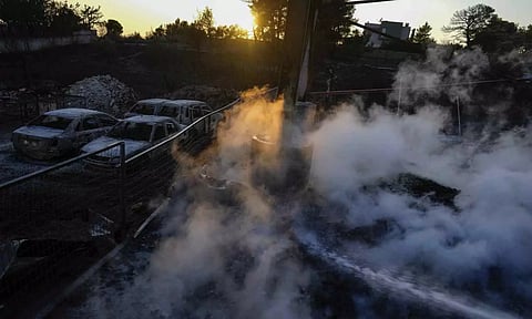Vapor rises as a firefighter sprays water near burned vehicles inside a damaged business in Penteli, a suburb of Athens (AP)