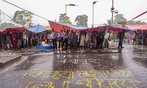 Agitators take cover during rains as junior doctors continue their 'cease work' and sit-in demonstration against the RG Kar Hospital incident, outside Swasthya Bhavan in Kolkata (PTI)