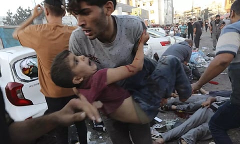 An injured Palestinian boy is carried from the ground following an Israeli airstrike outside the entrance of the al-Shifa hospital in Gaza City (AP)