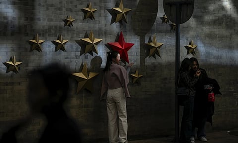 A beam of sunlight is cast on a woman as visitors take souvenir photos with the communist symbol of stars on display along a street in Beijing (AP)