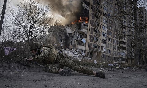 A Ukrainian police officer takes cover in front of a burning building that was hit in a Russian airstrike in Avdiivka, Ukraine (AP)