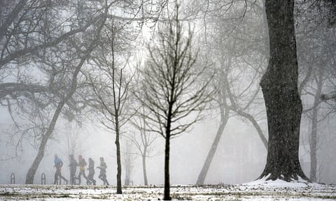 A group of people jog in the distance as heavy snow falls Sunday (AP)