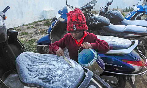 A child removes frost from a two-wheeler during a cold and foggy winter morning, at Ooty in Nilgiris district (PTI)