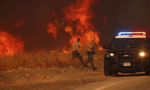 County Sheriff officers return to their vehicle after monitoring flames caused by the Hughes Fire along a roadside in Castaic (AP)