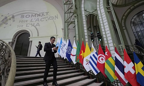 A man looks at his mobile phone as he walks past flags during an Artificial Intelligence Action Summit at the Grand Palais in Paris (AP)