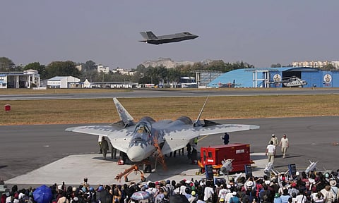 A U.S. Air Force fighter aircraft F-35 flies over Russia’s Su-57 fighter aircraft, parked at the static display area, on the fourth day of the Aero India 2025 (AP)