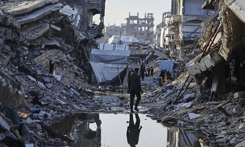 Palestinians walk amid the rubble of destroyed homes (AP)