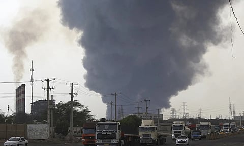 A black smoke rises in the sky as vehicles drive on the road after a massive explosion rocked a port near the southern port city of Bandar Abbas (AP)